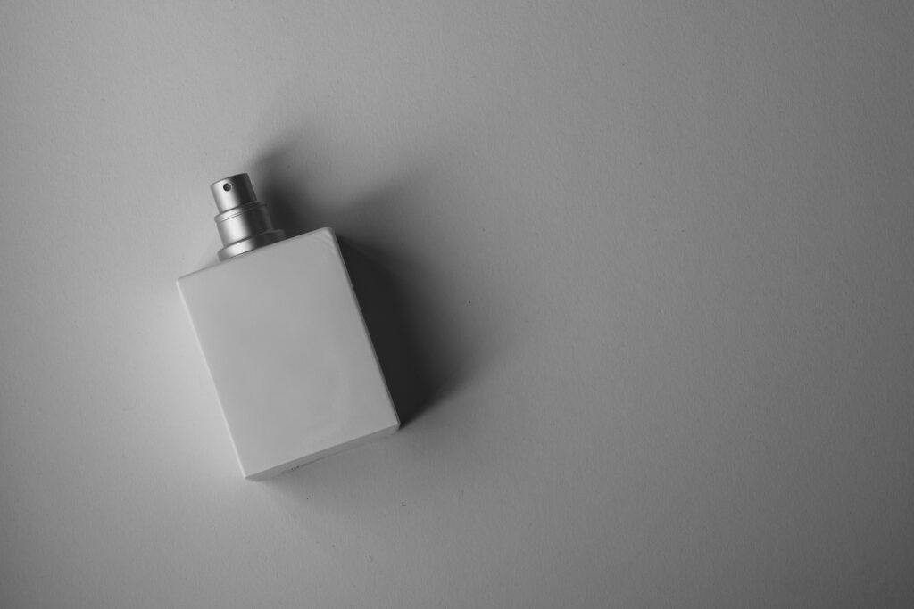 A sleek white perfume bottle photographed on a gray background with soft, muted lighting.